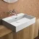 Waschtisch in Weiß von Ideal Standard, mit wandmontiertem Wasserhahn und rechteckiger Form, auf einer Holzoberfläche vor einer Korkwand installiert.